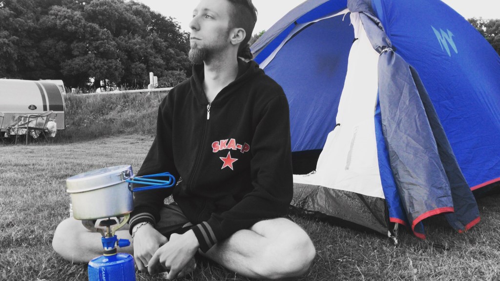 Andrea seduto accanto alla tenda blu con il fornelletto acceso, in un campeggio dell’Isola di Wight