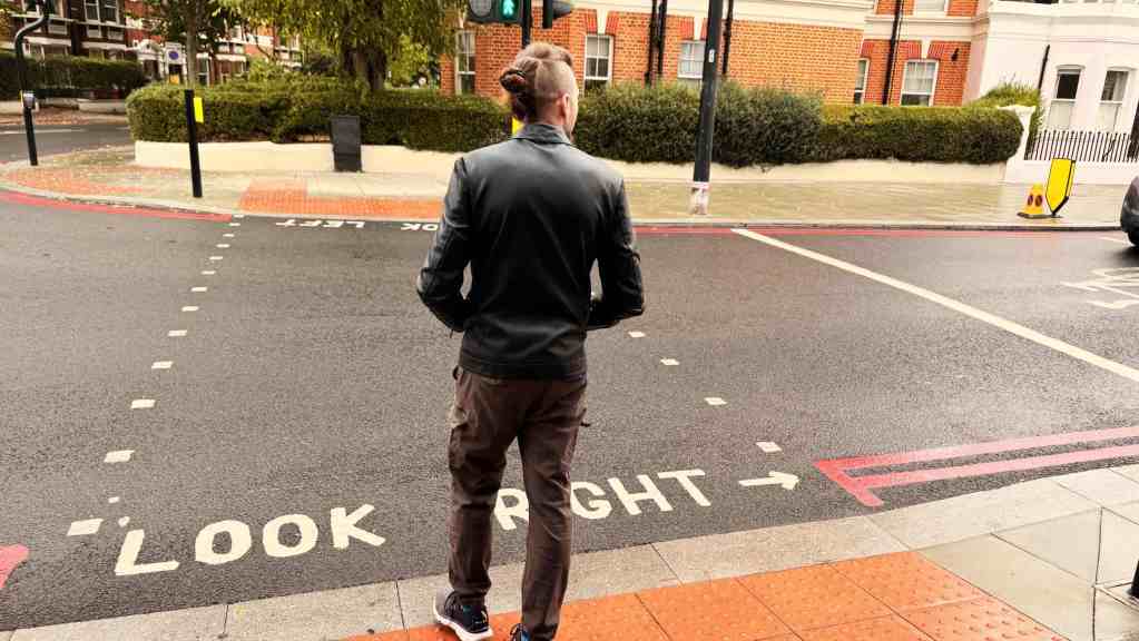 Andrea di spalle sul bordo del marciapiede, davanti alla scritta LOOK RIGHT dipinta sull’asfalto di una strada di Londra